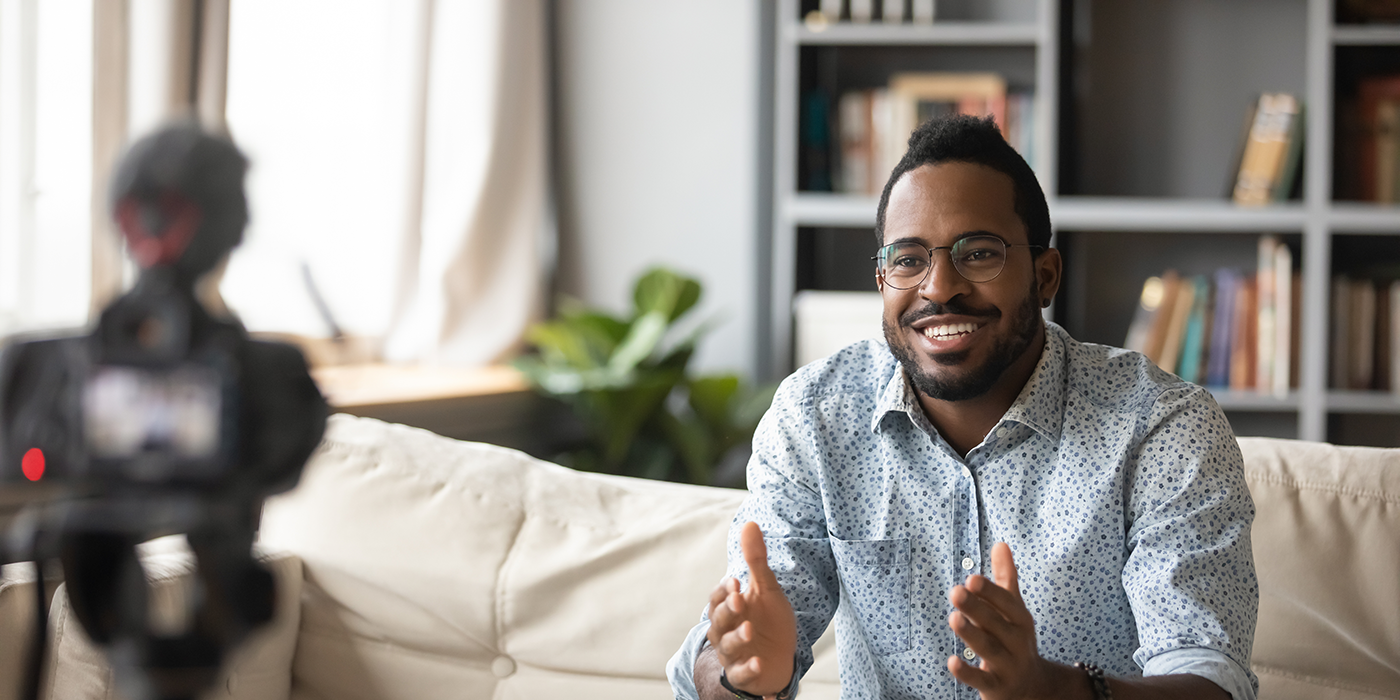 A man on a couch recording a video from a camera on a tripod