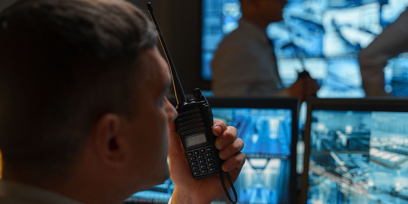 A man holding up a walkie talkie while observing surveillance video screens