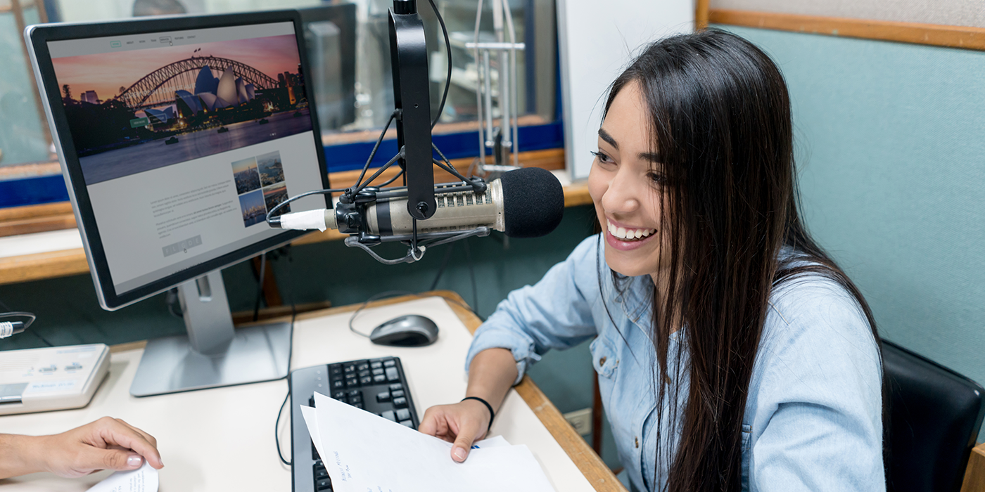 A woman in front of a computer with an image of Sydney Harbor on the screen