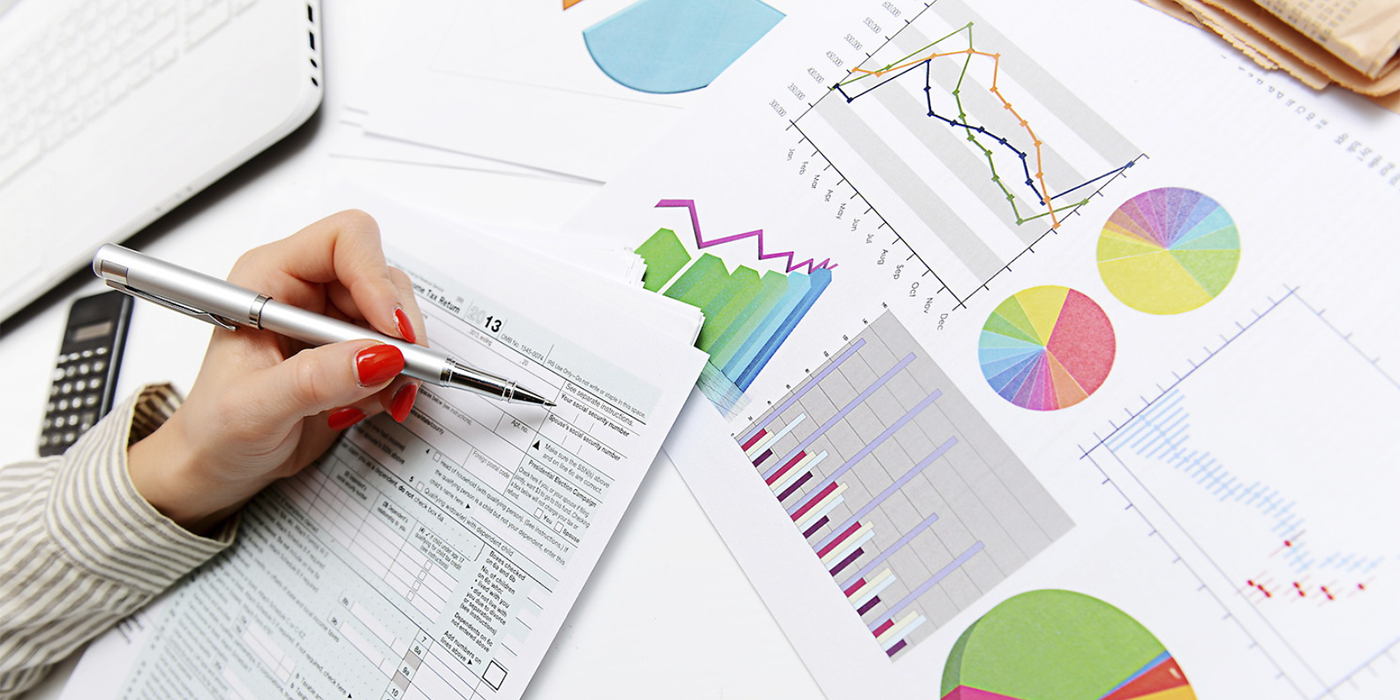 A hand holding a pen over a series of charts and forms